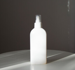 White cosmetic spray bottle mockup on white table and grey background. Sun rays. Shadow.