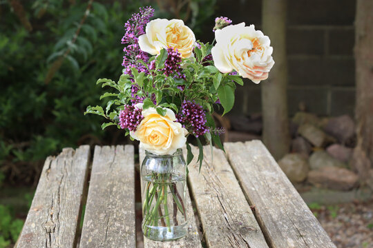 Reuse Glass Jam Jar for a vase of flower. Recycle Reuse Reduce concept. Jar Vase of enemies , rose, buddleia flower on old wooden table. 