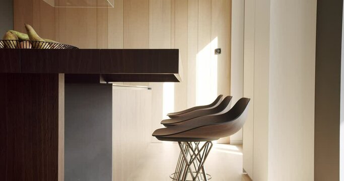 Detail in kitchen studio interior, modern island with countertop and wooden bar stools. Stylish apartment with contemporary furniture and design. Minimalist style.