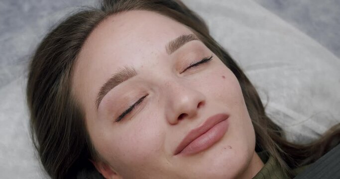 Beautiful woman client lying in beauty salon after eyebrow permanent makeup pleased by result. closeup on female face after brow correction procedure. Microblading eyebrow tattoo