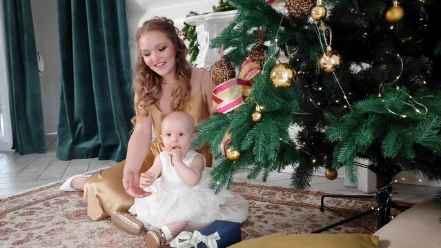 A beautiful mother with a little daughter in her arms decorates the Christmas tree in the living room. New Year's gifts under the tree. large bright room prepared for Christmas. sweet family. High qua