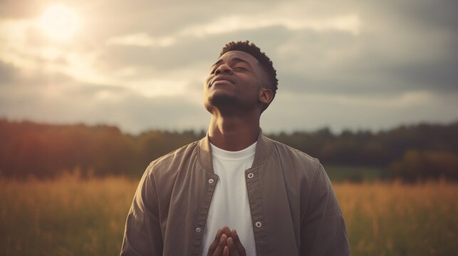 A young black African man, spiritual and reflective, praying in a sunlit field, gazing upwards, captured with natural lighting and desaturated tones.