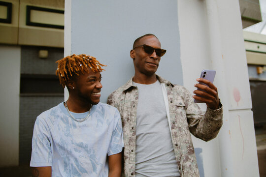 Two fashionable black men posing in urban area with their phone