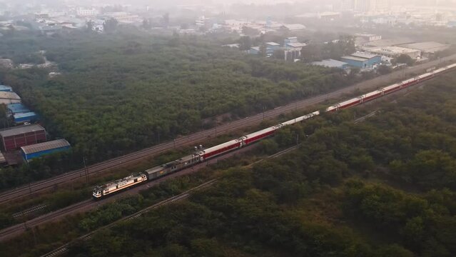 A passenger train passes through a forest in a stunning aerial shot of India's railway system, showcasing the natural beauty of a developing nation.