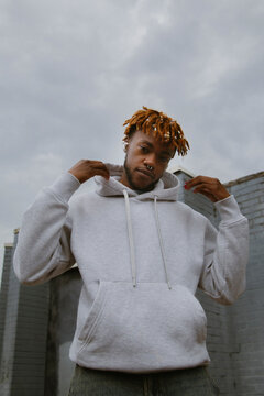 Young queer black man in street style outfit and ear pods posing in urban area