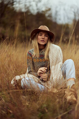 Portrait of a beautiful girl, sitting in the field, posing for the camera, wearing a hat, covered in a cardigan.