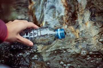 A female hand, filling up the bottle with water, in nature, from the sources. - obrazy, fototapety, plakaty