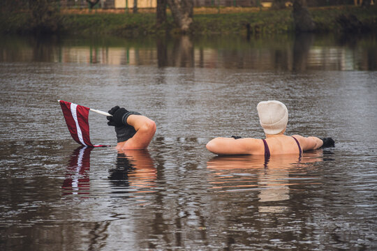 Couple ice bathing in the cold water of a lake in Preili, Latvia on the independence day. Wim Hof Method, cold therapy, breathing techniques, yoga and meditation
