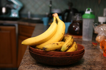 A bunch of bananas lying on a solid kitchen table. Sweet ripe bananas with yellow skin. Kitchen Scene with Bananas and Mixed Fruits Hand of ripe bananas in kitchen countertop
