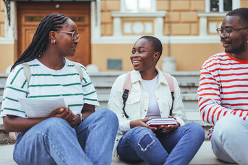 Happy young interracial students chatting with each other after class standing outside. Guy and...