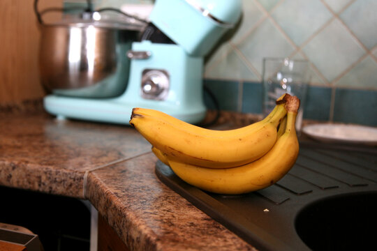A bunch of bananas lying on a solid kitchen table. Sweet ripe bananas with yellow skin. Kitchen Scene with Bananas and Mixed Fruits Hand of ripe bananas in kitchen countertop