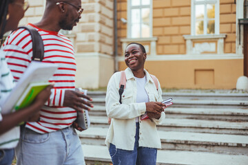 Happy young interracial students chatting with each other after class standing outside. Guy and...