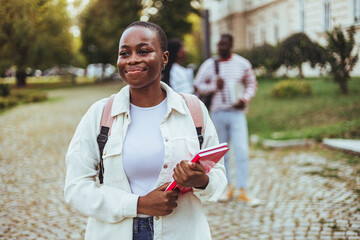 Portrait of happy African American lady student posing with laptop in hands outdoors, looking and...