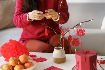 Asian Woman decorated house for Chinese New Year Celebrations. putting traditional pendant to the...