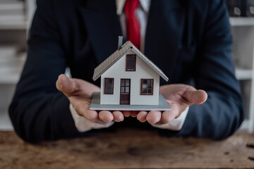 Real estate agent holds a model of a house offered to his client after signing the sales contract at the office. Real estate investment concept and businessman's hands holding wooden model