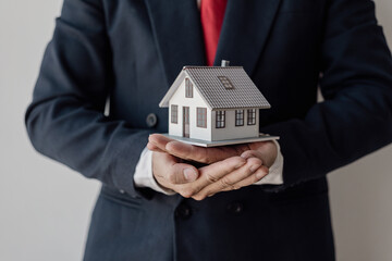 Fototapeta na wymiar Real estate agent holds a model of a house offered to his client after signing the sales contract at the office. Real estate investment concept and businessman's hands holding wooden model