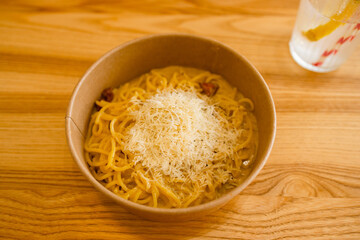 Yellow pepper pesto spaghetti covered with grated cheese in a eco paper bowl on a wood background at city cafe. High quality photo