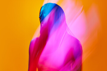 Portrait of young woman posing against orange studio background with neon colored reflection on body. Concept of art, modern style, cyberpunk, futurism and creativity