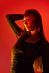 Portrait of young beautiful girl posing against orange studio background with neon reflection on...