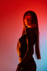 Portrait of young beautiful girl posing against orange studio background with neon reflection on...