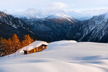 Lonely wooden house on snowy meadow surrounded by orange larch forest in Italian Alps. Monte Bianco...
