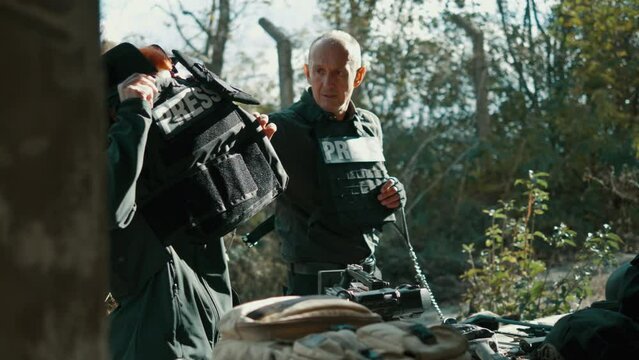 War journalists,  man, and woman, take off their bulletproof vests and army helmets after completing their work at a war zone