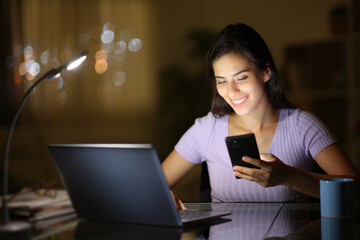 Happy woman using laptop and phone in the night at home - obrazy, fototapety, plakaty
