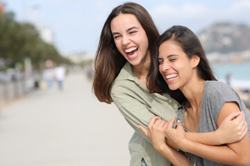 Two happy friends hugging and laughing outdoors - obrazy, fototapety, plakaty