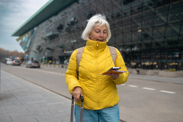 Tourist is waiting a taxi. Senior woman stand outside airport and wait for taxi cab after vacation...