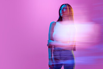 Portrait of young elegant woman in casual clothes posing against light purple background in neon...