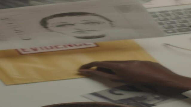 Vertical top view of African American police detective looking at printed suspect identikit while investigating criminal case late in office