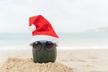 Santa Claus Watermelon wears stylish sunglasses on the sand contrasting with the sea. wearing a...