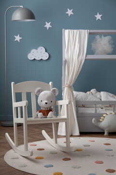 Creative composition of cozy kid room interior with stylish bed, round rug, white chair, plush bear, stars ornament, gray lamp, ornament on wall and personal accessories. Home decor. Template.