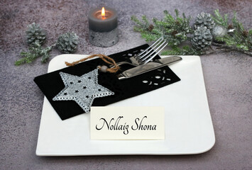 Candles with fir branches and table setting. With the text Nollaig shona on a place card.
