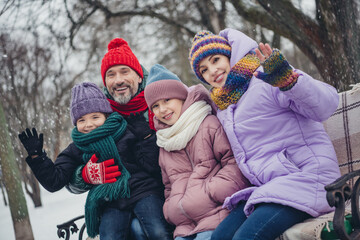 Fototapeta na wymiar Portrait of full friendly family sitting bench chilling arm waving hi snowfall weather outside