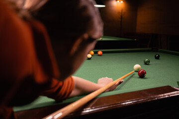 Woman with cue pointing at billiard ball at table. Playing billiards concept - obrazy, fototapety, plakaty