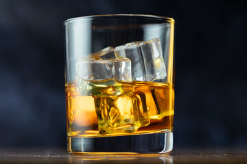 A glass of whiskey and ice old polished table on dark background