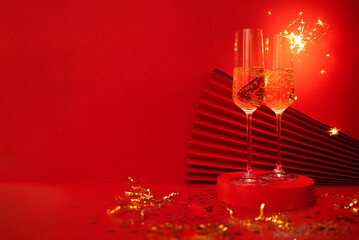 Two glasses of champagne on a podium. Carnival mask and paper fan on a bright red background