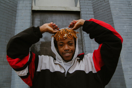 Portrait of African man wearing hoodie posing in urban area smiling into camera with arms up