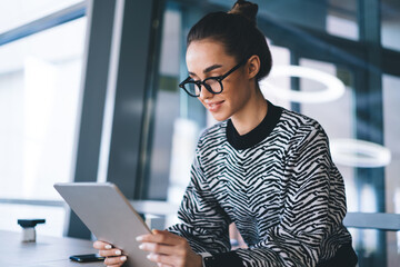 Focused positive young woman using tablet in office