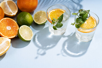 Summer orange cocktails with citrus fruits on blue background. Hard seltzer, lemonade, refreshing drinks, low alcohol mocktails, summer party concept. Trendy palm leaf shadow and sunlight, sun.