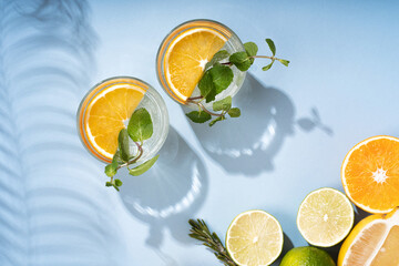 Two glasses of summer orange cocktails with citrus fruits on a blue background. Lemonade, refreshing drinks, low alcohol cocktails, summer party concept. Fashionable shade of palm leaves and sunlight.