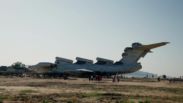 an abandoned white plane is standing on a sandy beach, tourists are walking around. bright blue sky on the background, slow motion, smooth movement of cameras from right to left, wide shot