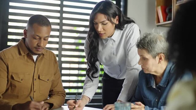 Motivated transgender woman team leader explaining company development strategy to smiling young diverse colleagues. 