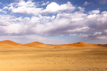 Selective focus morning view of desert landscape with red dunes under  soft white clouds in blue sky, Sossusvlei, Namibia