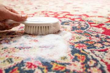 Male hand holding a white brush, on a natural fiber rug with white foam, abstract texture, soft...