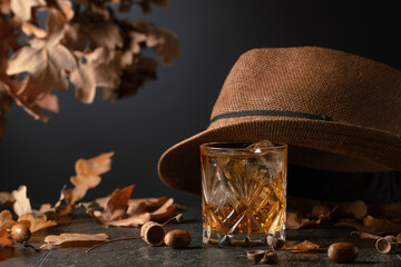 Whiskey with ice on a stone table with dried oak leaves.