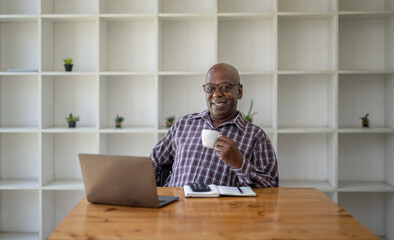 Senior black man taking a coffee break while working on a laptop.