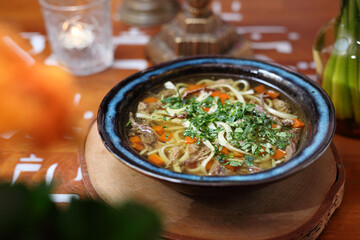 Broth with meat and homemade noodles, sprinkled with fresh parsley. Soup in a bowl, on a wooden table. 