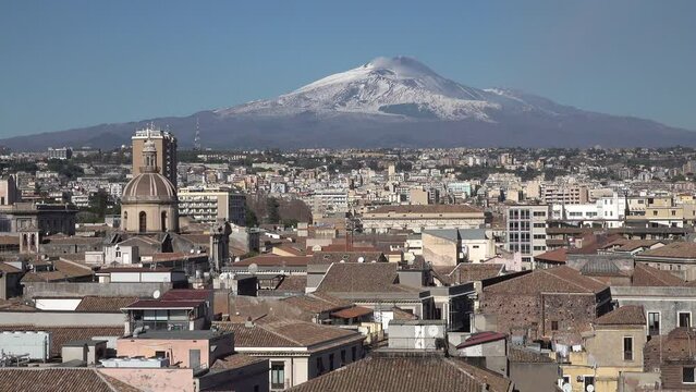 Establishing shot of historic city center of Catania contrasting with looming Mount Etna volcano on Sicily, Italy
